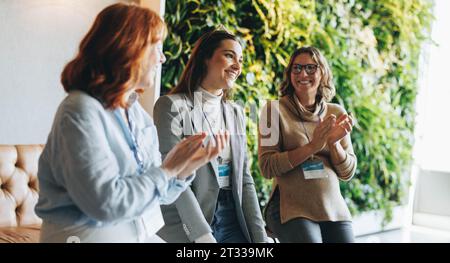 business women applaud and smile during a successful meeting in an office conference room. They demonstrate teamwork and collaboration in this product Stock Photo