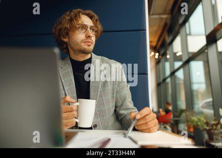 Focused businessman working on project while using laptop and making notes while sittting in office Stock Photo