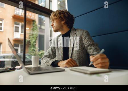 Handsome businessman working on project while using laptop and making notes while sittting in office Stock Photo