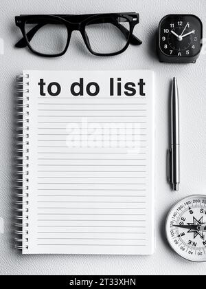 "To do list" words on blank notepad page with pen, black glasses, clock and compass on white background, vertical style. Empty line page notebook for Stock Photo