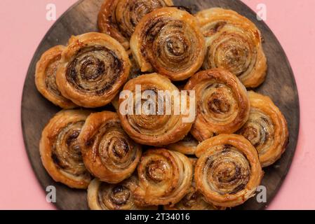 Freshly baked sweet and crispy cinnamon rolls. On a wooden plate and pink background Stock Photo