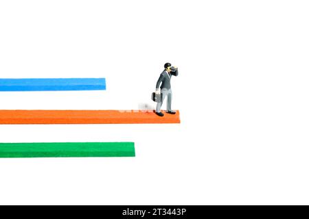 Miniature tiny people toy figure photography. Progress monitoring concept illustration. A businessman using binocular telescope standing above multipl Stock Photo