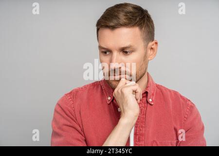 Sad pensive thoughtful man touching chin looking down isolated on gray background. Stock Photo