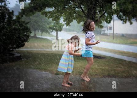 Sisters jumping in puddles during summer rain Stock Photo