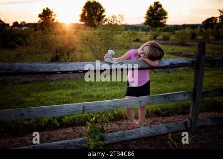 Young child smiling at stuffed lamb toy in sunny field Stock Photo