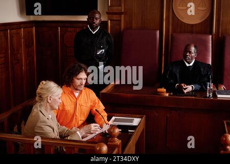 Confident mature attorney explaining case point to defendant during presentation and discussion of juridical document in courtroom Stock Photo