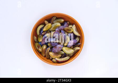 Sweet and ripe pieces of plums in a brown color clay bowl on white background. Stock Photo