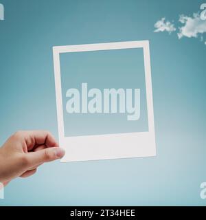 Female hand holding a vintage instant photo, copy space, blue sky in the background Stock Photo