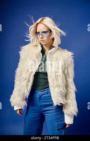 charming woman in white faux fur jacket, hat and sweater posing on grey ...