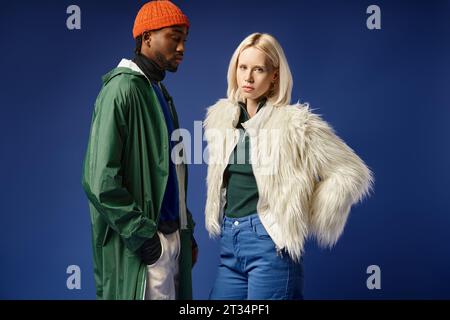 beautiful woman posing with african american man in winter attire of blue backdrop, diverse models Stock Photo