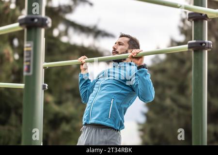 Young man working out calisthenics in an outdoor gym using parallel bars. He does push-ups on the bar. Concept of healthy lifestyle. Stock Photo