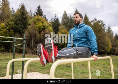 A young athlete trains on the bars, raises his legs parallel to the bars, strengthens his stomach and legs. Stock Photo