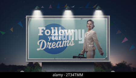Confident vintage style businesswoman on billboard advertisement and motivational quote: follow your dreams Stock Photo