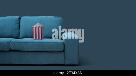 Popcorn box on the couch: TV, movies and entertainment concept Stock Photo