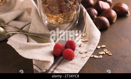 Couple of glasses of chocolate and chestnuts mousse with roasted almonds and oats decorated with raspberries and mint leaves. Stock Photo