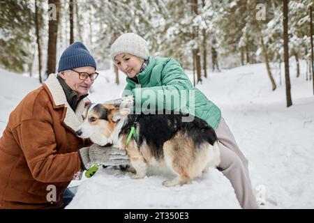 Happy senior couple spending time with corgi dog in winter park Stock Photo