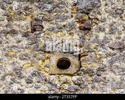 Small round ventilation hole and ends of timber beams making a 'funny face' in old stone wall - central France. Stock Photo
