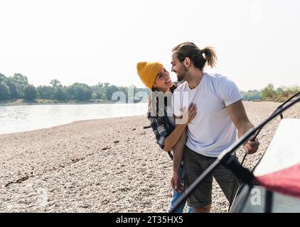 Happy young couple setting up a tent at the riverside Stock Photo