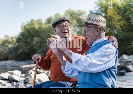 Two old friends sitting by the riverside, having fun Stock Photo