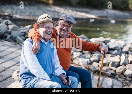 Two old friends sitting by the riverside, having fun Stock Photo