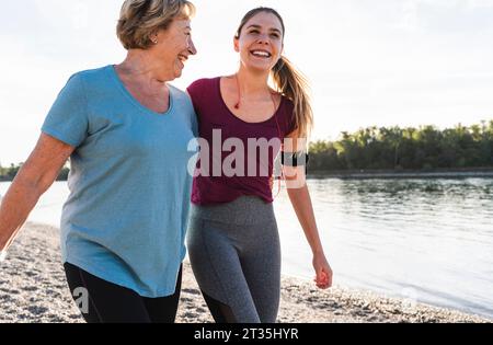 Fit grandmother and granddaughter walking at the river with arms around, having fun Stock Photo