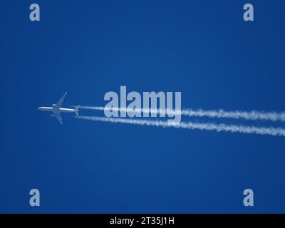 Tele close-up of an airliner flying at high altitude with contrails in a clear blue sky Stock Photo