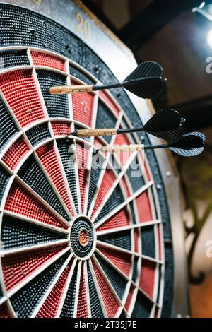 Three black darts hitting the dartboard in bar Stock Photo