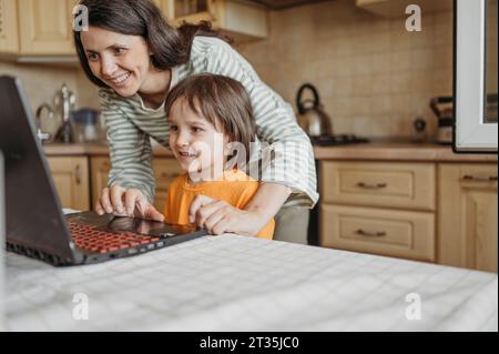 Smiling mother assisting son learning through laptop at home Stock Photo