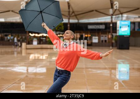 Carefree woman dancing with umbrella in city Stock Photo