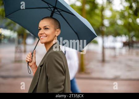Smiling woman with shaved head holding umbrella Stock Photo