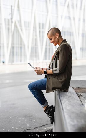 Woman using tablet PC sitting on by road in city Stock Photo