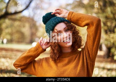 Cheerful redhead woman wearing knit hat at autumn park Stock Photo