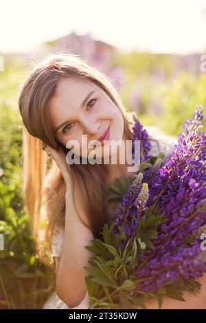 Smiling woman holding bunch of purple lupine flowers Stock Photo