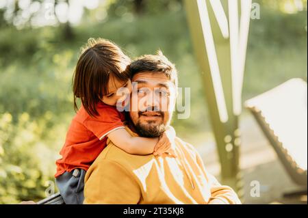 Smiling son embracing father sitting at park Stock Photo