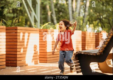 Carefree boy playing with bubbles in park Stock Photo
