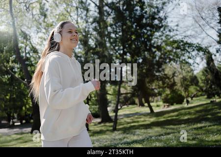 Teenage girl listening music with headphones jogging at park Stock Photo