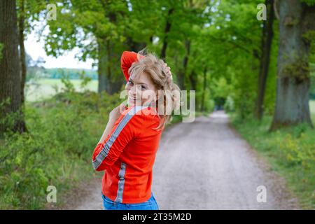 Smiling woman standing on footpath amidst trees Stock Photo