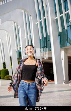 Happy student listening to music and walking in front of university building Stock Photo