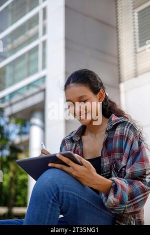 Smiling student using tablet PC sitting outside university Stock Photo