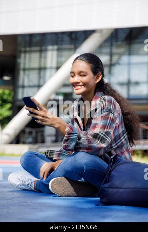Smiling student using smart phone in front of university Stock Photo