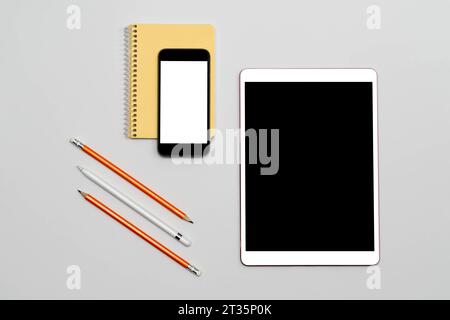 Tablet and phone with isolated screen, notepad, pencils lying on table. Minimalism mockup with white isolated screen. Education concept. Online Work a Stock Photo