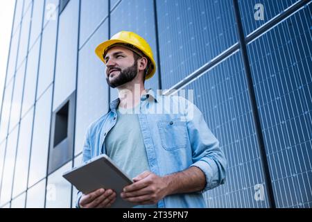 Contemplative engineer holding tablet PC in front of solar panels Stock Photo