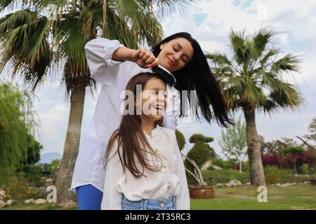 Happy woman combing hair of daughter in park Stock Photo