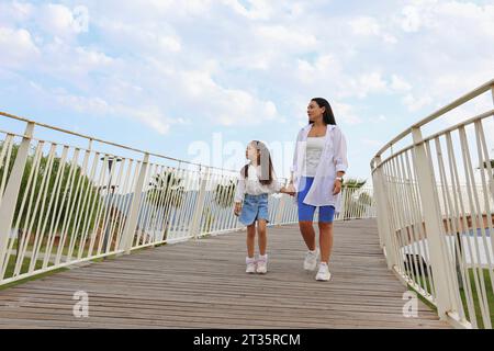 Mother and daughter holding hands and walking on bridge Stock Photo