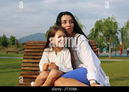 Smiling girl sitting with mother on lounge chair in park Stock Photo
