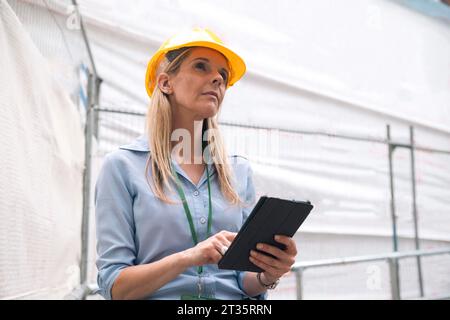 Contemplative engineer looking up holding tablet PC Stock Photo