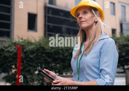 Thoughtful engineer holding tablet PC in front of building Stock Photo