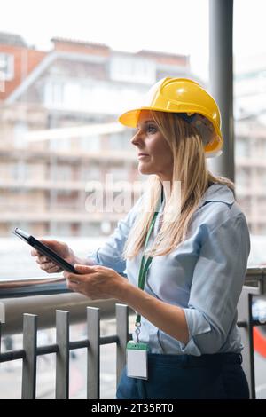 Contemplative businesswoman holding tablet PC leaning on railing Stock Photo