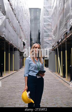 Thoughtful engineer holding hardhat standing at construction site Stock Photo