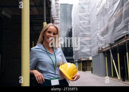 Happy engineer leaning on pole at construction site Stock Photo